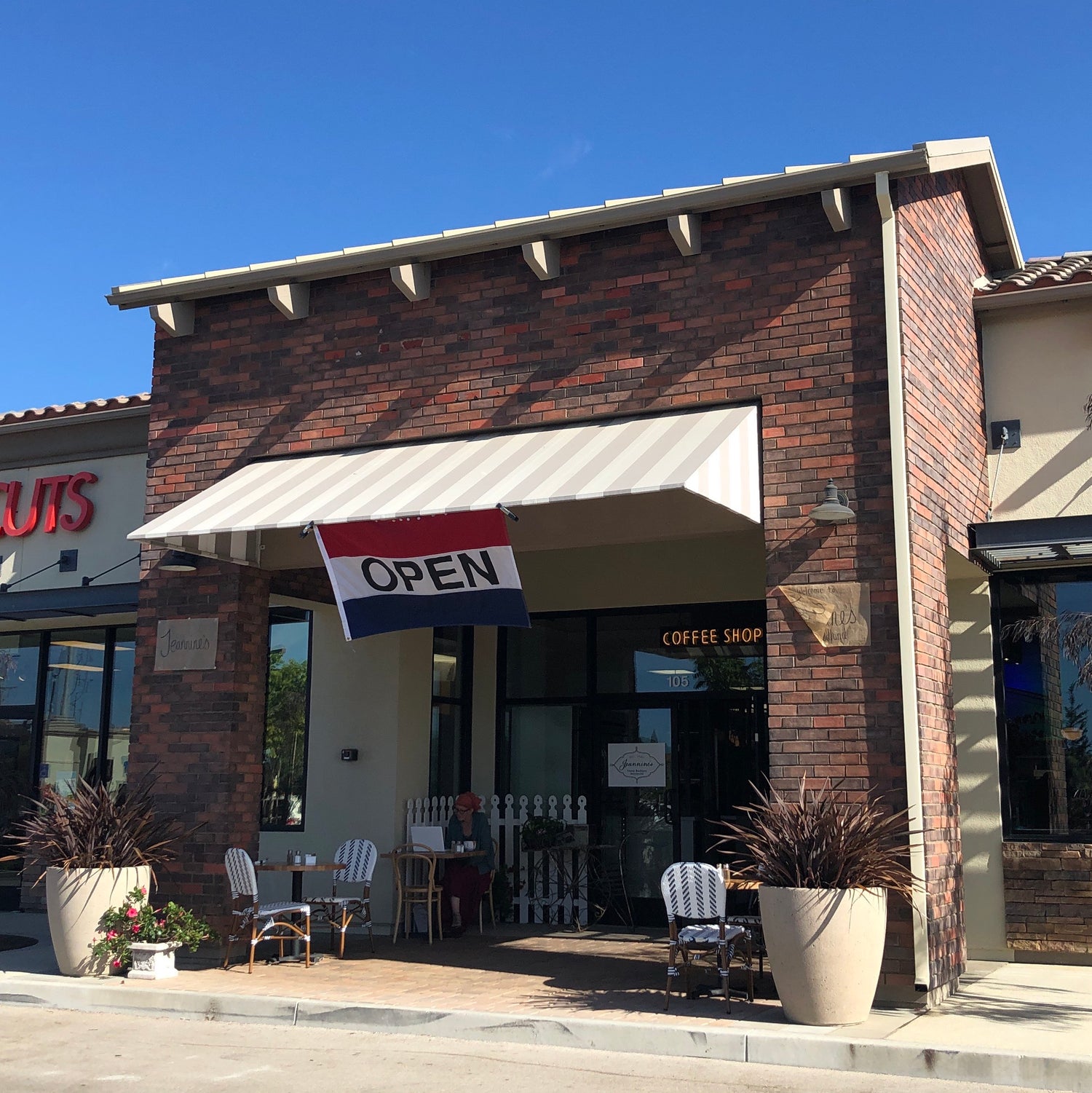 Jeannine’s Goleta exterior with brick facade, striped awning, “OPEN” flag, and outdoor café seating.