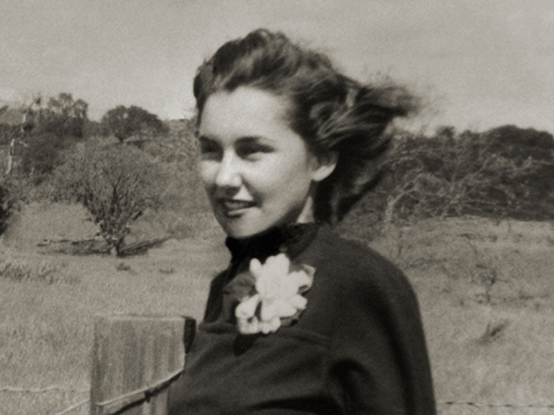 Black and white photo of Eleanor Hardey by a fence, with windswept hair and a flower on her dark top.
