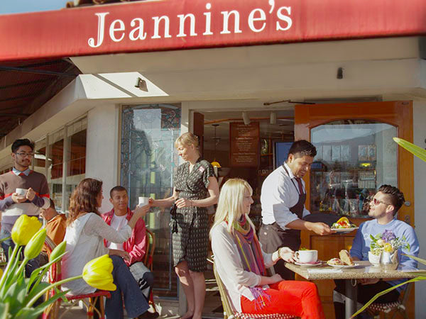 Sunny outdoor seating at Jeannine’s café with servers, guests, yellow tulips, and red awning overhead.